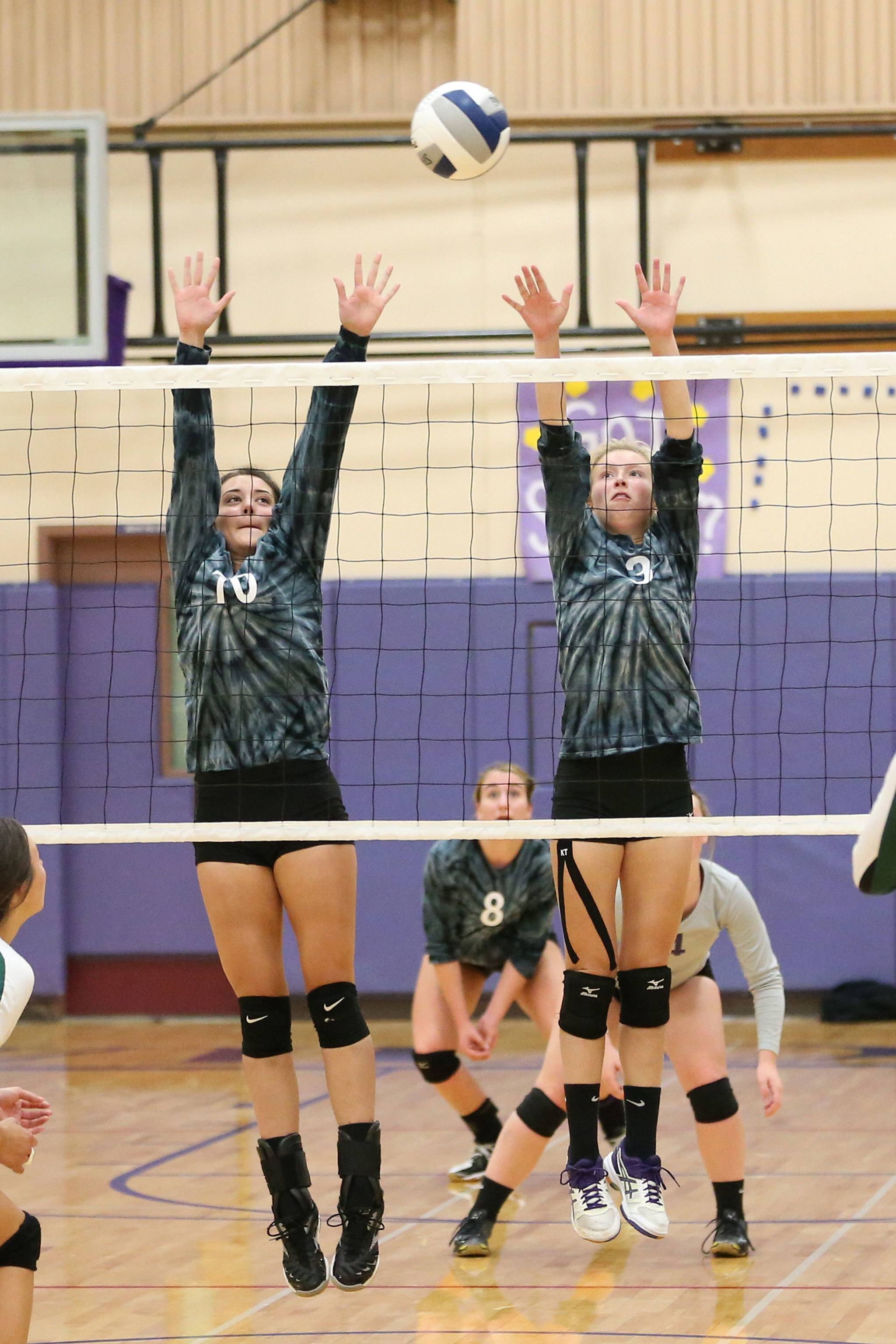 Kristina Tirado, left, and Cami Bristow rise to block for Oak Harbor. (Photo by John Fisken.)