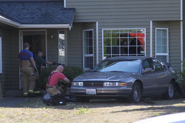 Firefighters with the Oak Harbor Fire Department  help clean up debris and glass caused by a car that struck a house in reverse at S.W. Kittitas Court Friday morning.
