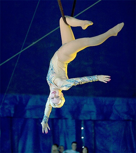 A circus acrobat wows the crowd with dozens of aerial stunts as she flies high in the air.