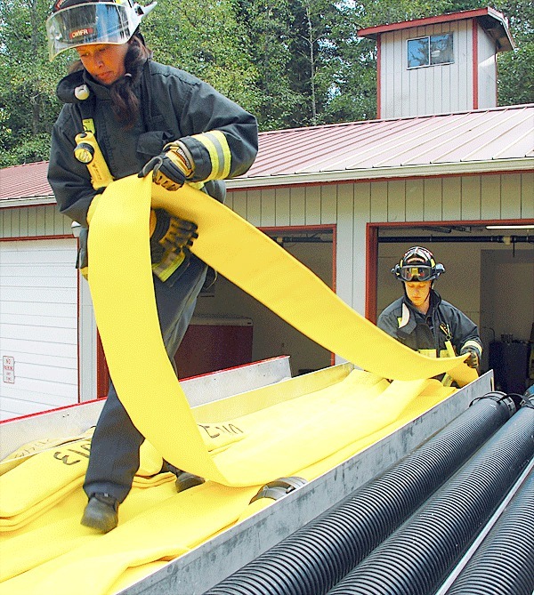 Central Whidbey Fire and Rescue firefighters Leah Kalahiki and Kevin Moberg fold fire hose on top of a water tender at Station 52 on Morris Road. A lack of district volunteers is driving the station’s closure.