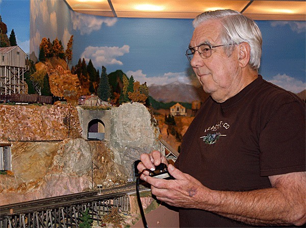 Jack Tingstad holds a controller for one of his electric engines next to his model railroad.