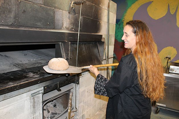 Kelly Baugh removes a loaf of bread from her brick wood-fire oven.