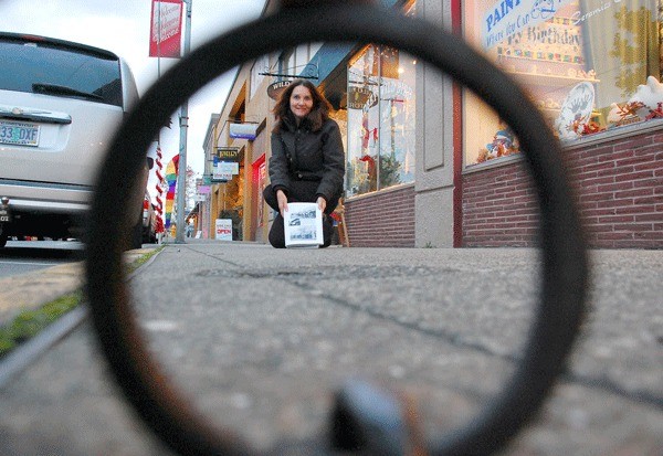 Amateur historian Peggy Darst Townsdin holds up a 1920s photograph of horses pulling wagons down SE Pioneer Way. She and many others believe a single metal ring in a sidewalk in front of Paint Your World was once used to tie up horses. Oak Harbor officials have promised to preserve the ring when new sidewalks are put in next year.