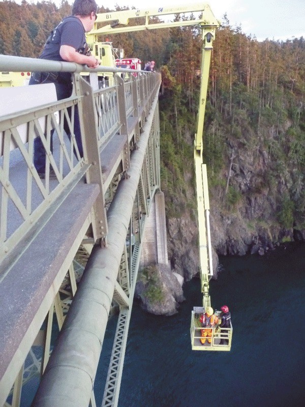 A North Whidbey Fire and Rescue firefighter and a Washington Department of Transportation worker are lowered over the side of Deception Pass Bridge to retrieve two Mill Creek residents who attempted to cross the bridge along its underside girders.