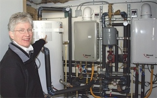 Janet Hall points out the household hot water storage tank – not to be confused with an energy-wasting “water heater.”  This 80-gallon tank stores water warmed by rooftop passive solar tubes.  The solar-heated water circulates to their in-floor radiant heating system and also serves their other domestic hot water needs.