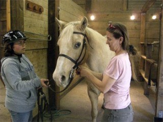 Wildwood Farm barn manager Fonda Ligget helps a young rider bridle a horse before a lesson.