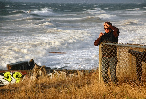 A woman holds onto her hood Friday while taking pictures of waves on West Beach Road. The windstorm was the first of the season to reach gale-force conditions.