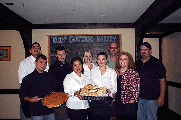 The restaurant staff stands in front of bakery shelves showing off freshly baked rolls and a famous giant pancake.