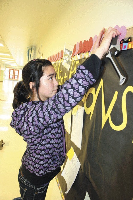 Sixth-grader Rickell Piloneo hangs paper hearts in the hallway of her school for the new donations Wednesday.
