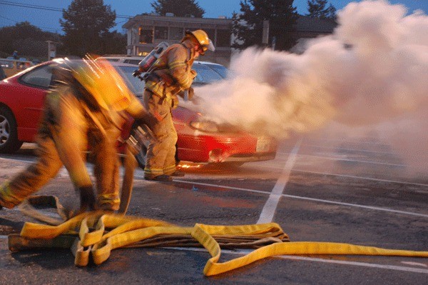 Two firefighters from the Oak Harbor Fire Department begin attacking a car fire that broke out in front of Safeway Friday