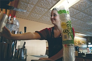 Angelo’s Caffe barista Toni Leyden stocks biodegradable cups at the coffee counter. Downtown Oak Harbor businesses are making a push to implement “green” practices.