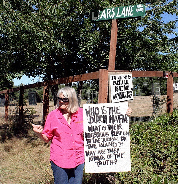 Central Whidbey resident Carol Magee stands with the signs she placed on her property bordering Houston Road. To irritate her neighbors