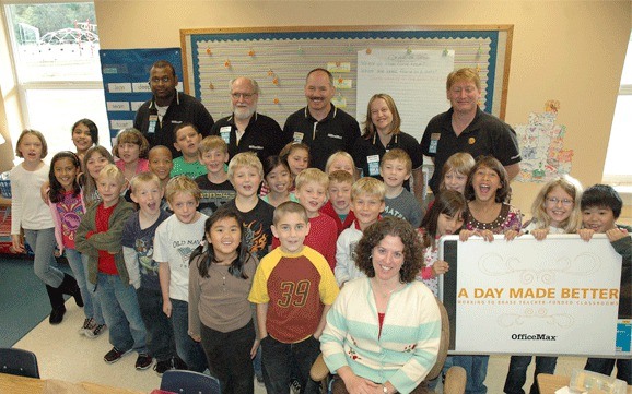 Teacher Nicole Bouvion sits in her new leather office chair surrounded by her third graders. In the back are OfficeMax employees Rubin Cavitt