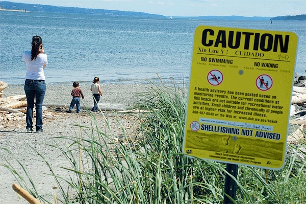 A mother watches her two children play on a beach at Windjammer Park this past June despite it being closed due to pollution. Oak Harbor had been planning to fix the problem this summer