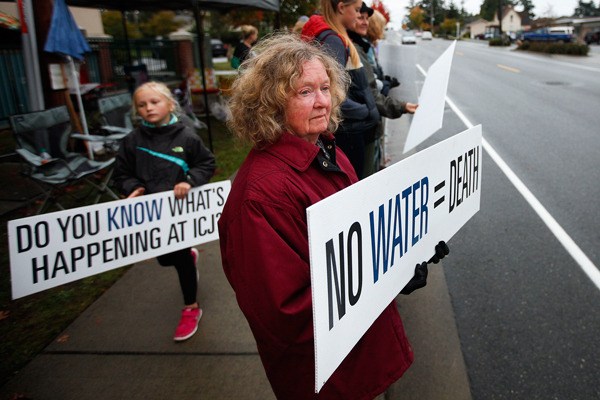 Vicki Morse (center) holds a sign outside of Island County Jail in Coupeville to mark the six-month anniversary of her grandson’s death from dehydration there on Wednesday