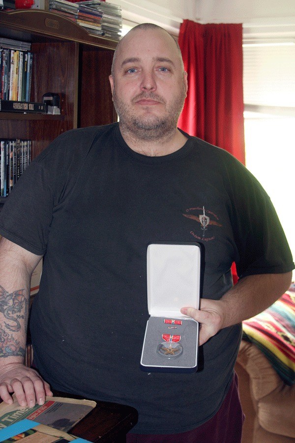 Dennis Skaggs holds up his Bronze Star medal in his Oak Harbor home more than 20 years after receiving it. RIGHT: Infantry soldier Skaggs during the Gulf War in 1991.