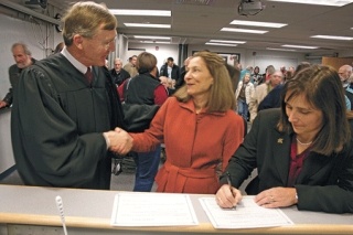 Judge Alan Hancock and newly officiated Island County Commissioner Angie Homola shake hands as Commissioner Helen Price Johnson signs her oath of office.