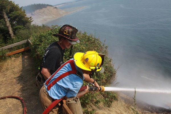 Firefighters with North Whidbey Fire & Rescue work to contain a brushfire climbing a steep bluff at Fort Ebey State Park Wednesday.
