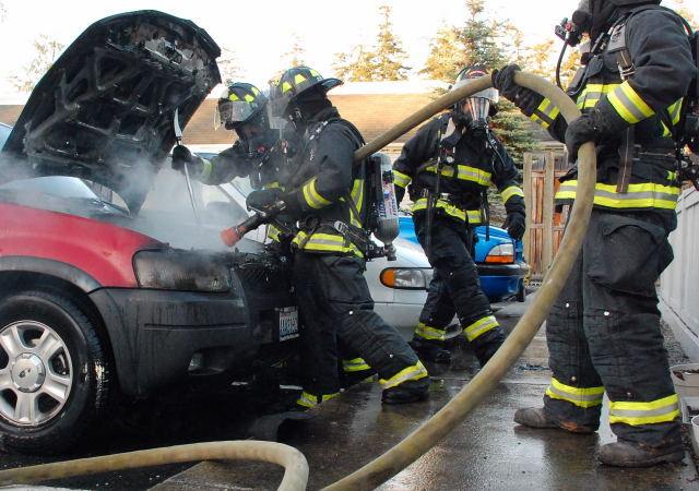 Central Whidbey Fire and Rescue firefighters hose down a vehicle on fire in Coupeville Monday