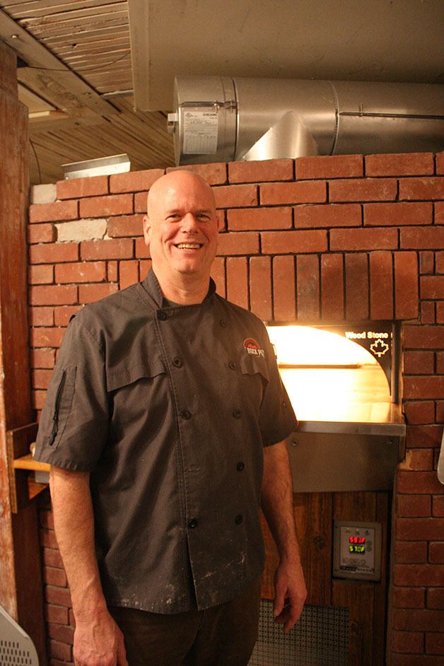 Oak Harbor restaurant owner Reid Schwartz stands in front of a gas-fired oven in Hot Rock Pizza. The name and logo he uses resulted in a threatening letter from The Rock Wood Fired Kitchen attorneys.