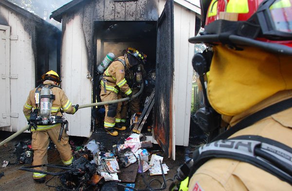 A team of Oak Harbor Fire Department firefighters hose down one of two outbuildings that were destroyed by fire Tuesday afternoon. The blaze is considered suspicious and is under investigation.