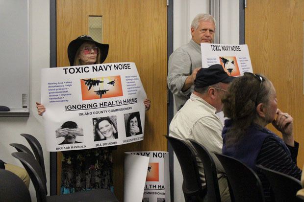 Anti-jet-noise activists hold signs at the Island County Board of Health meeting Tuesday.