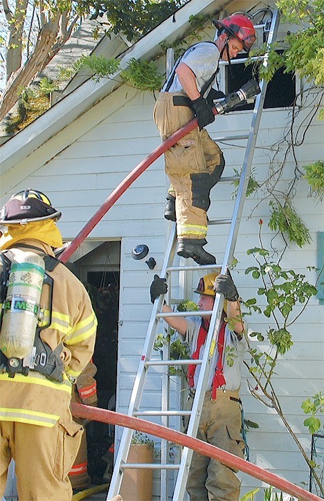 A firefighter descends a ladder after extinguishing the last embers of a fire that severely damaged a North Whidbey home Sunday.
