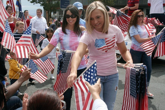 Representatives from RE/MAX Acorn Properties hand out flags to parade-goers along Pioneer Way.