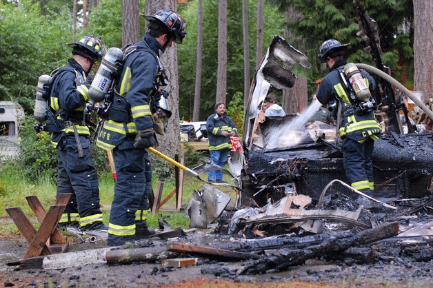 Central Whidbey Fire and Rescue firefighters Kevin Moberg and Jerry Helm watch as fellow firefighter David Mott douses the remains of a truck-camper fire near S. Quail Trail Lane.