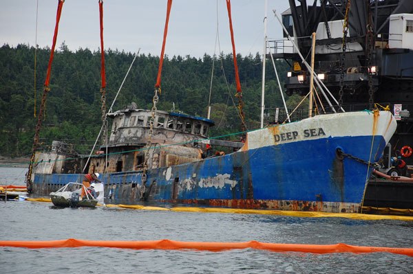 Workers lay down absorbent pads to soak up diesel fuel from the Deep Sea as it sits in its slings after being raised Sunday. The 128-foot crab boat sank in Penn Cove three weeks ago.