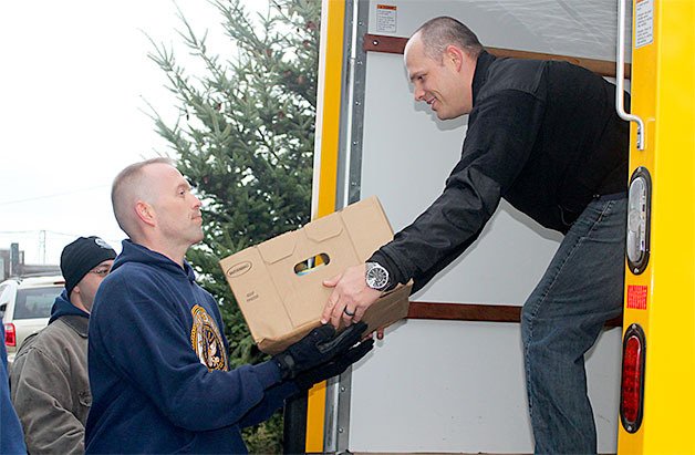 Petty Officer First Class Clayton Steckel hands Petty Officer First Class Jeffrey Arrowsmith a box of frozen turkeys as volunteers work to unload 320 frozen turkeys into the freezer at North Whidbey Help House.