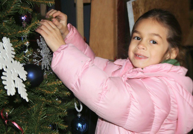 Seven-year-old Megan Croft hangs a snowflake ornament on a tree while helping her dad
