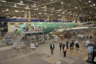Boeing officials at the Renton plant watch Tuesday as employees from the Commercial Airplanes division work on a P8-A plane resting on a moving production line.
