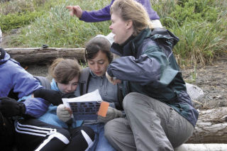Seventh-graders Maddy Mosolino and McKenzie Schneider along with parent Paige McGuire study tide pool charts while fighting off a chilly breeze.