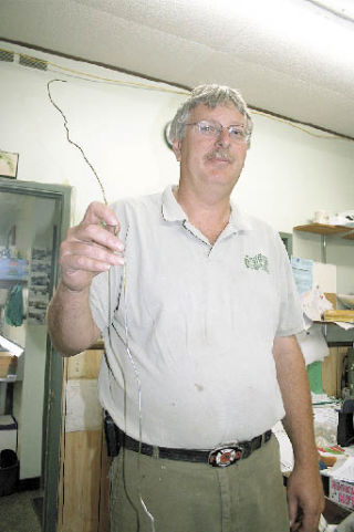 Greenhouse Florist and Nursery co-owner Henry Vandenhaak holds the bent hanger thieves used to fish bags of money out of the deposit slot on the business’s safe. The burglars got away with at least $3