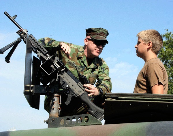 Master-at-Arms Seaman Peter Biloschaetzke talks to a boy on the roof of a military vehicle.