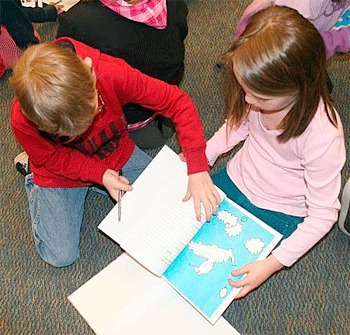 Students Sean Summers and Chelsea Hanson look through a copy of their book “Clouds Imagination in the Sky” at a book signing on June 14 at Olympic View Elementary.
