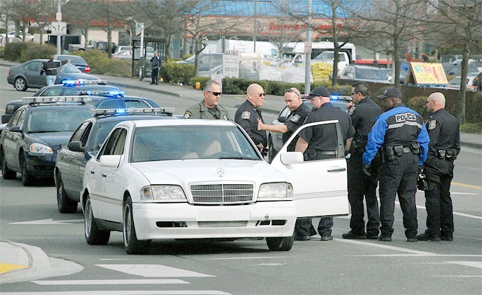 A group of police officers search a white Mercedes Benz after arresting four men suspected of rioting in Oak Harbor Monday afternoon.