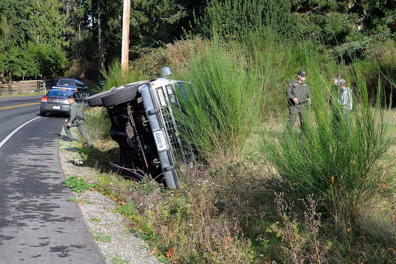 Reserve Deputy Kurt Pepper with the Island County Sheriff’s Office speaks with a driver who rolled her Suburban onto its side Thursday on Bayview Road.