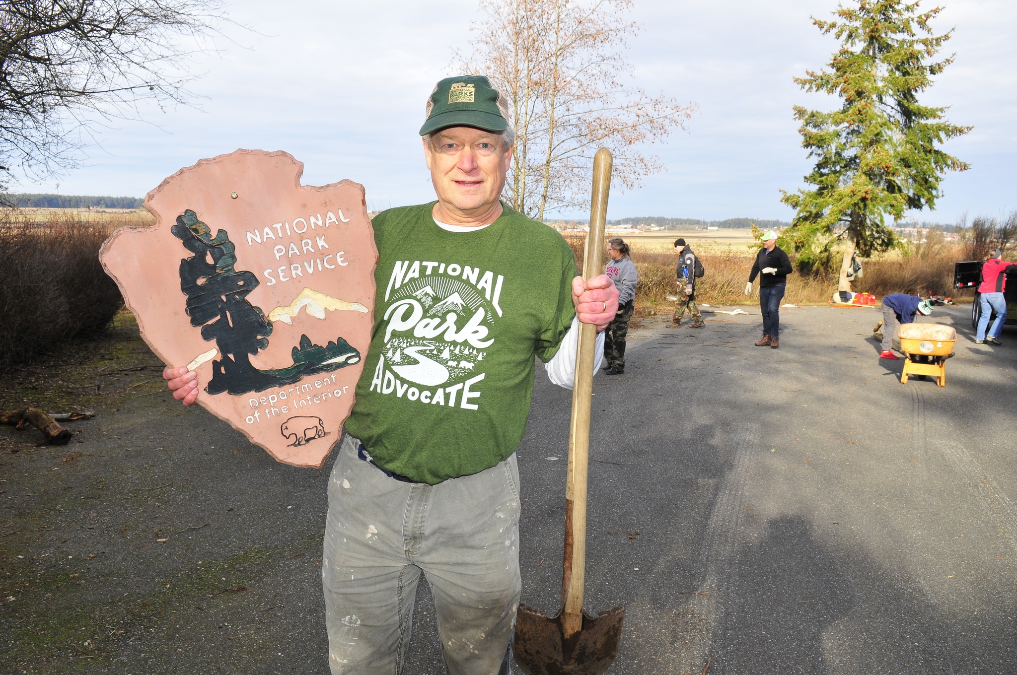 Rob Smith, a member of the National Parks Conservation Association holds up a dilapidated National Park Service sign and a broken shovel Monday, at Prairie Wayside in Coupeville, to show the condition of many things in need of repair or replacement in the National Park System. Smith and the NPCA were participating in a partner volunteer project along with Mission Continues, a veterans and active duty service members who spent their Martin Luther King holiday donating their time and work to the community. Photo by Michael Watkins/Whidbey News-Times
