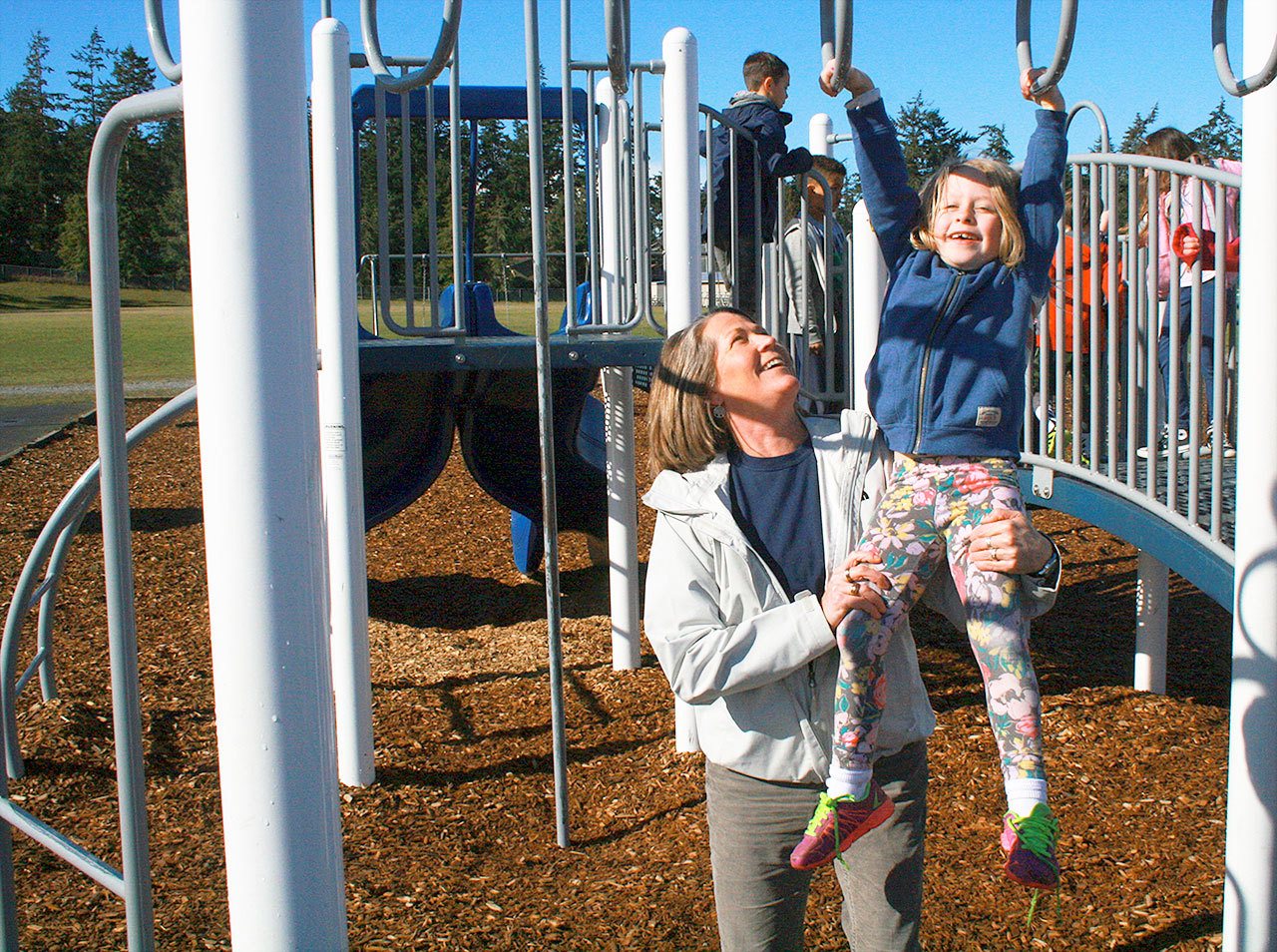Paula Seaman, principal of Hillcrest Elementary, helps first grader Milana Blatt cross the monkey bars during recess Wednesday in Oak Harbor. Photo by Daniel Warn