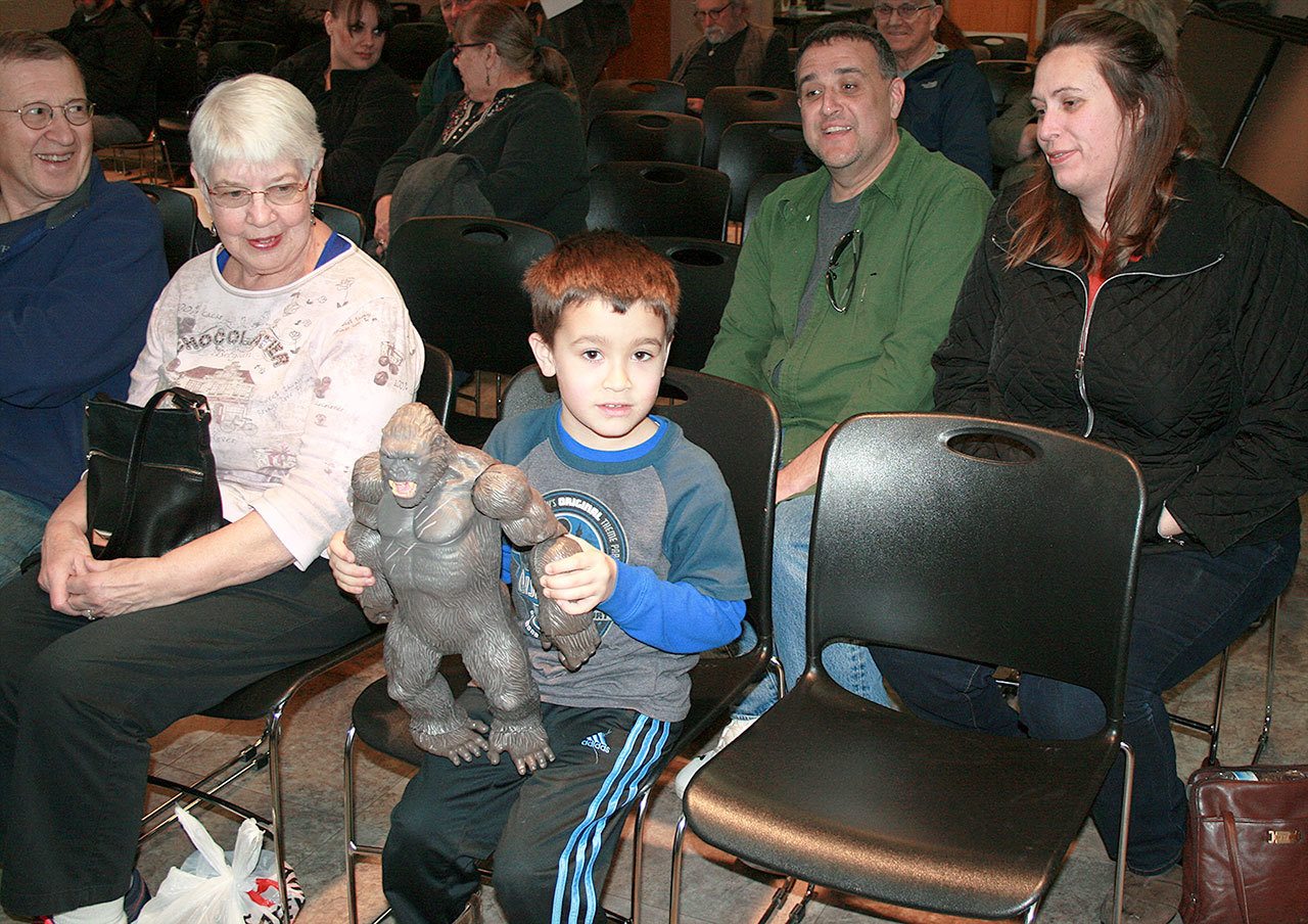 At Oak Harbor Library’s Sasquatch talk, Brayden Meadows, center, shows off his “King Kong” doll, which he imagines is Sasquatch. His parents, Jason and Carrie Meadows, right, supervise. Photo by Daniel Warn/Whidbey News-Times