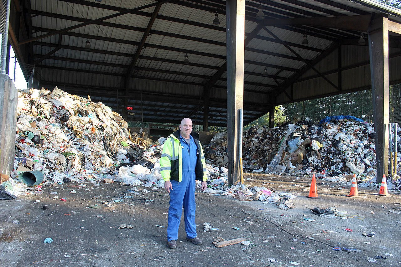 Todd Davis, lead technician at Island County’s Solid Waste Facility near Coupeville, stands in front of record heaps of garbage that normally is cleared out daily. It piled up because of a paralyzing ice storm in southcentral Washington last month. Photo by Patricia Guthrie/Whidbey News-Times