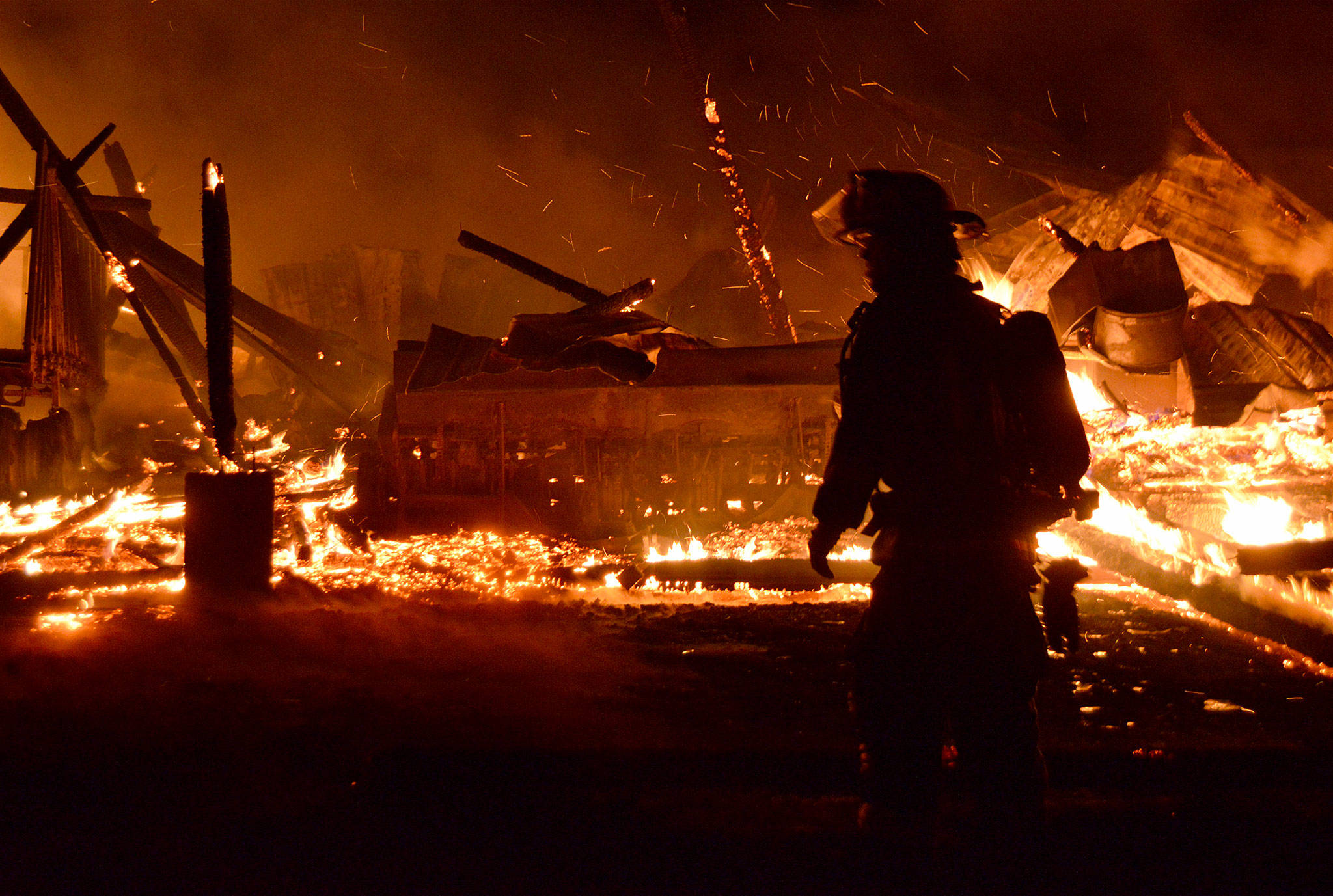 A firefighter is silhouetted against the burning remains of the historic Smith Barn on Ebey’s Prairie. Photo by Megan Hansen/Whidbey News-Times.