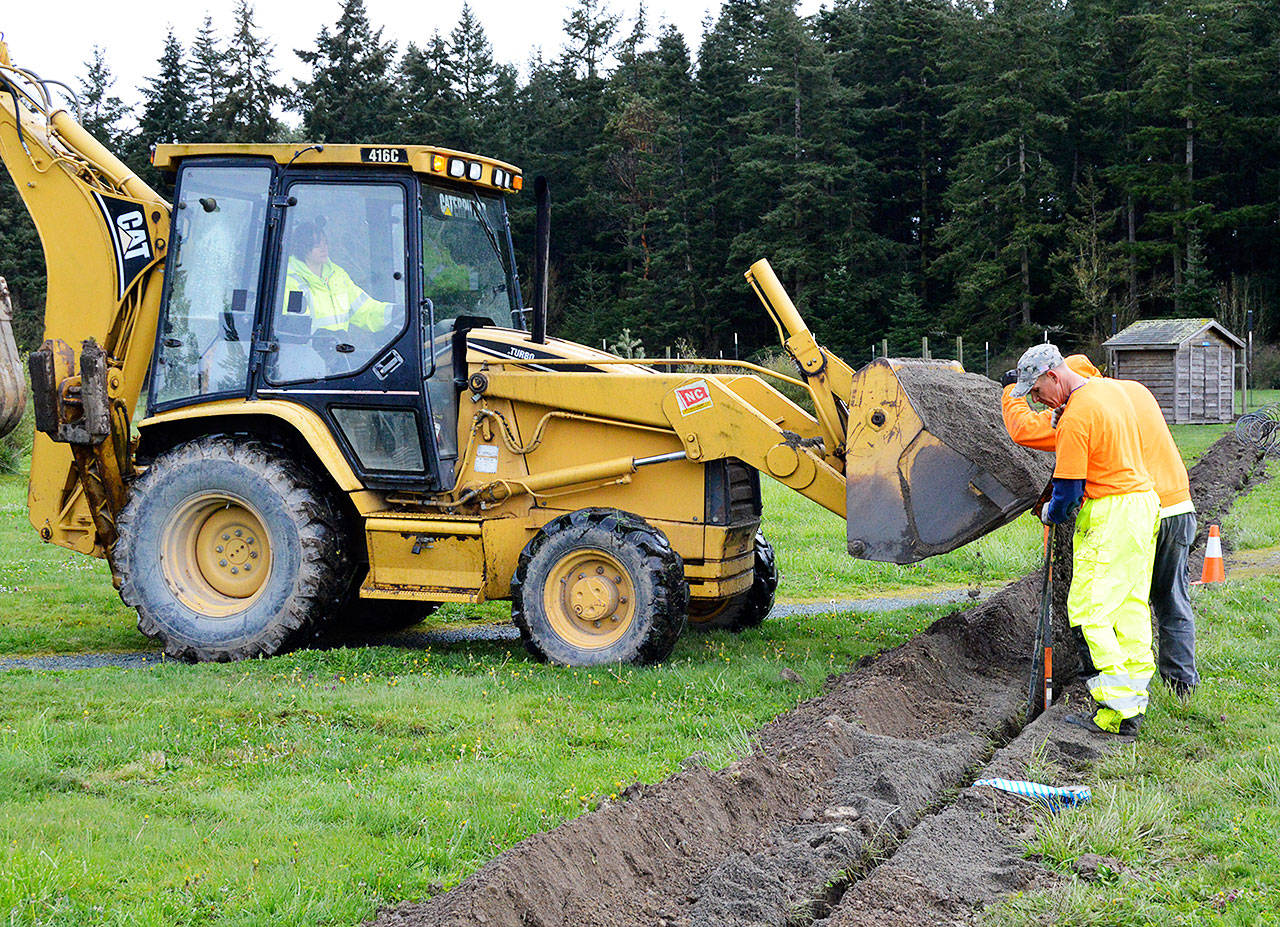 Public Works Superintendent Kelly Riepma uses a backhoe to drop dirt into a trench as public works employees Jimmy Wadlington and Scott Wofford cover a new water line going out to the community garden. Photo by Megan Hansen/Whidbey News-Times.