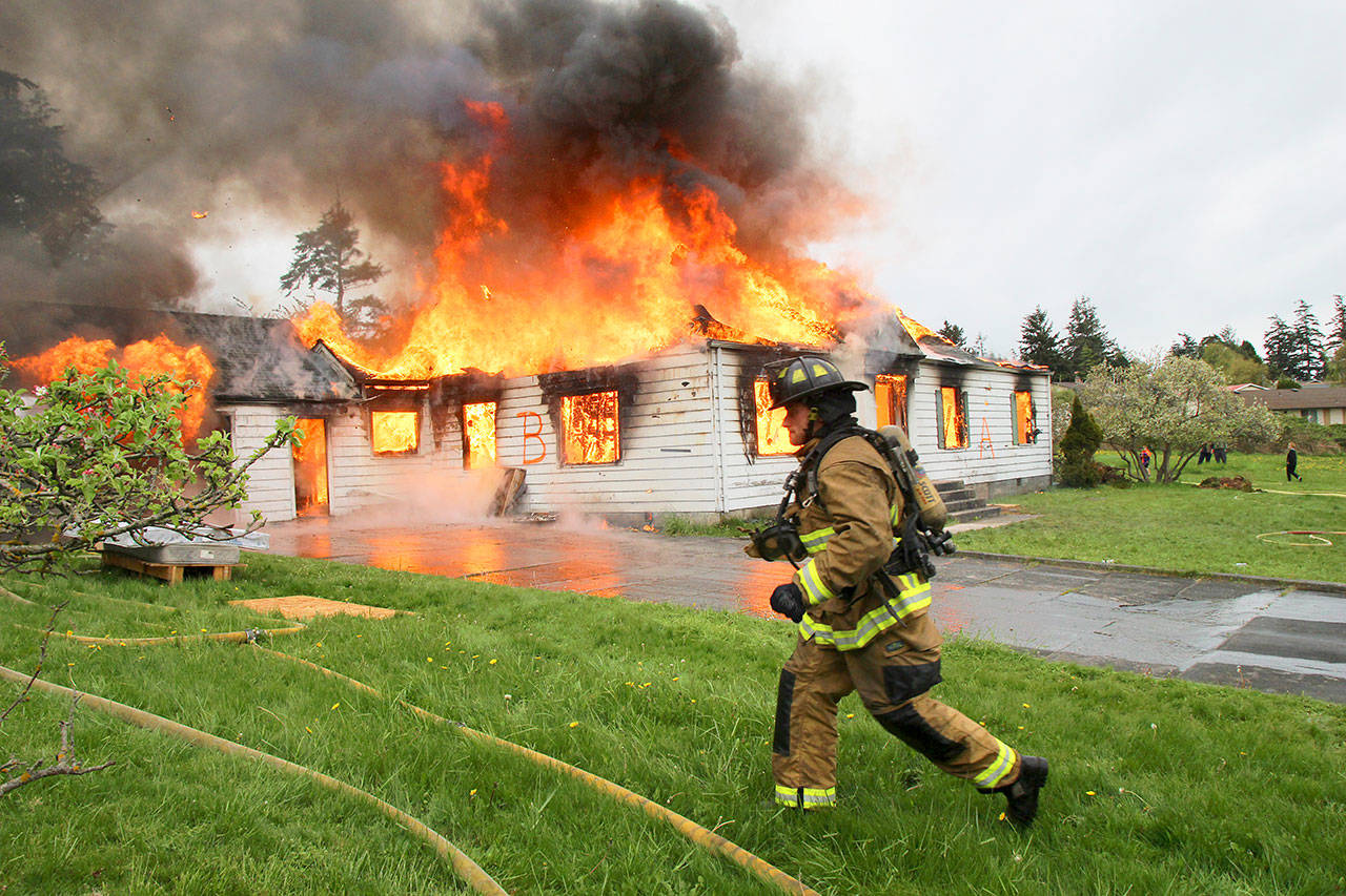Photo by Jessie Stensland / Whidbey News-Times                                A firefighters hurries by a house in flames during a burn on the west side of Oak Harbor last weekend.