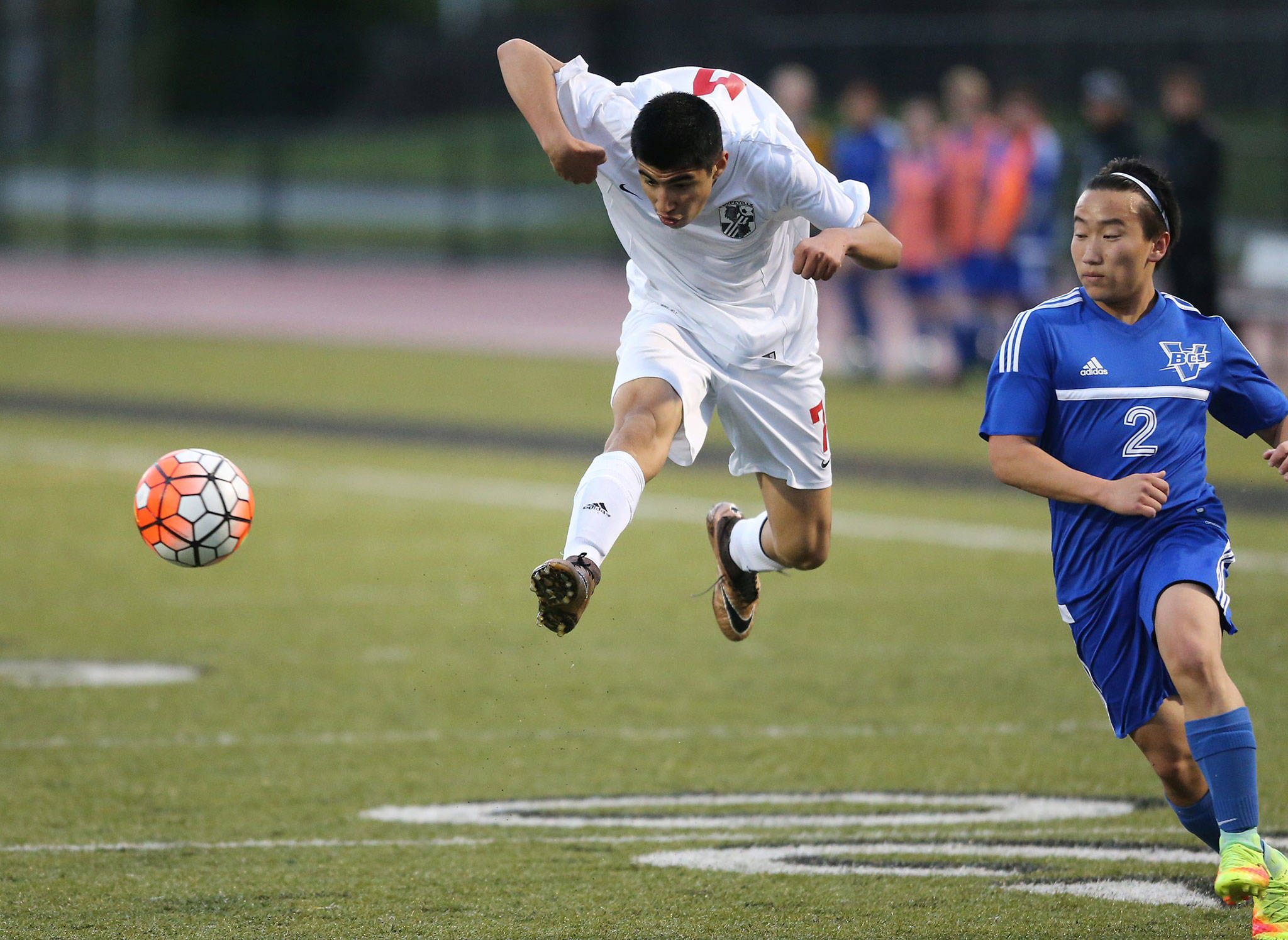Aram Leyva jumps to kick the ball as Bellevue Christian’s John Kim closes in. (Photo by John Fisken)