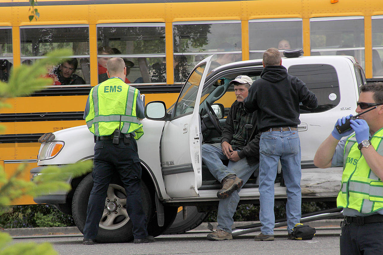 A hit-and-run accident on South Main Street in Coupeville leaves Coupeville&rsquo;s Greg Odle to contemplate what happened while emergency responders with WhidbeyHealth EMS and Central Whidbey Fire & Rescue tend to him as a school bus passes Thursday. Odle was uninjured. The driver who fled on foot was later found in a nearby field and arrested and booked into the Island County jail. Pictured in reflective vests are WhidbeyHealth EMS personnel Greg Behan, left, and Robert May, right. Next to Odle is firefighter/EMT Marvin Raavel. Photo by Ron Newberry/Whidbey News-Times