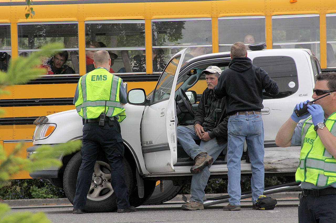 A hit-and-run accident on South Main Street in Coupeville leaves Coupeville’s Greg Odle to contemplate what happened while emergency responders with WhidbeyHealth EMS and Central Whidbey Fire & Rescue tend to him as a school bus passes Thursday. Odle was uninjured. The driver who fled on foot was later found in a nearby field and arrested and booked into the Island County jail. Pictured in reflective vests are WhidbeyHealth EMS personnel Greg Behan, left, and Robert May, right. Next to Odle is firefighter/EMT Marvin Raavel. Photo by Ron Newberry/Whidbey News-Times