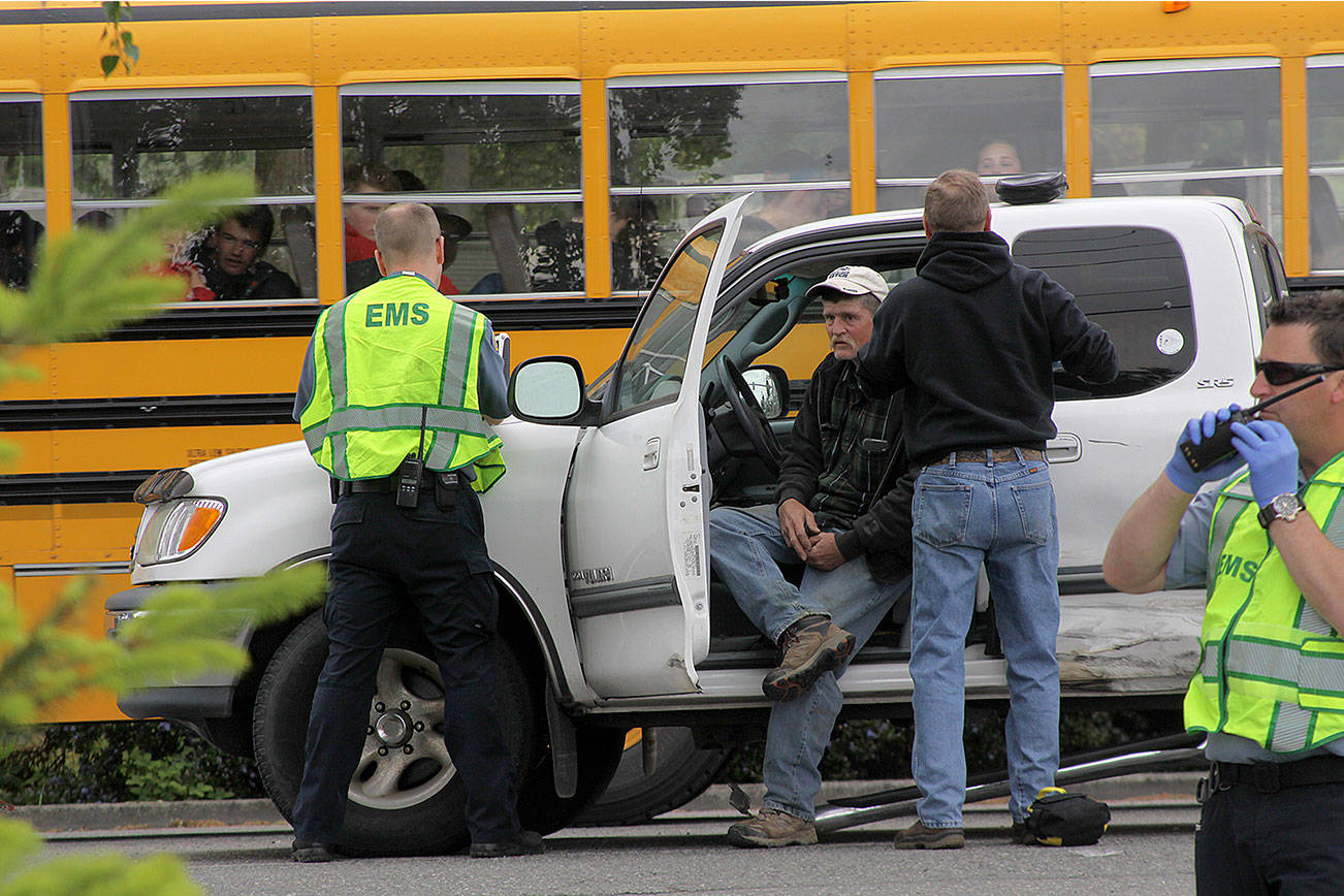 A hit-and-run accident on South Main Street in Coupeville leaves Coupeville’s Greg Odle to contemplate what happened while emergency responders with WhidbeyHealth EMS and Central Whidbey Fire & Rescue tend to him as a school bus passes Thursday. Odle was uninjured. The driver who fled on foot was later found in a nearby field and arrested and booked into the Island County jail. Pictured in reflective vests are WhidbeyHealth EMS personnel Greg Behan, left, and Robert May, right. Next to Odle is firefighter/EMT Marvin Raavel. Photo by Ron Newberry/Whidbey News-Times